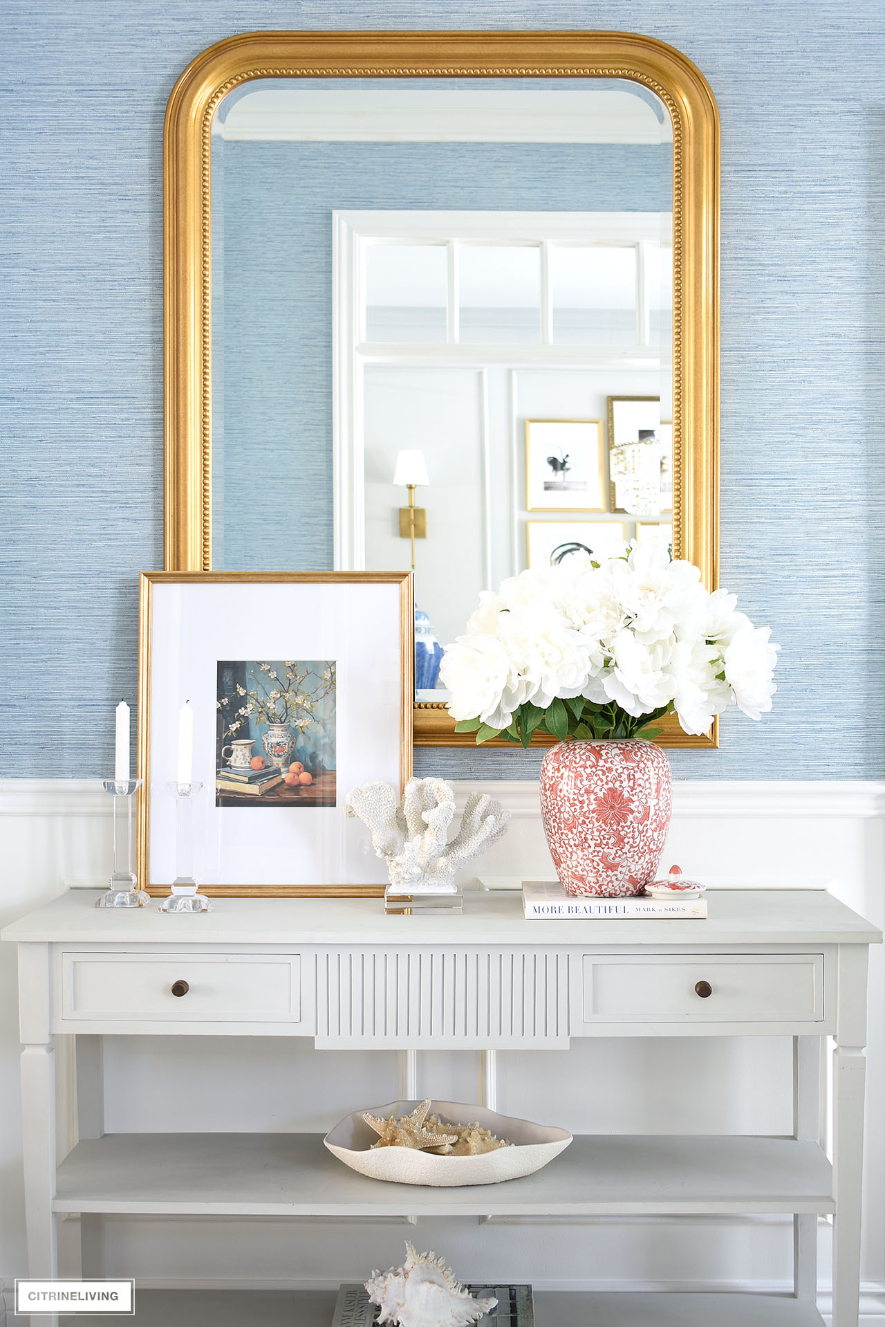 Entryway console table with faux peony arrangement, vintage art, coral and candles.