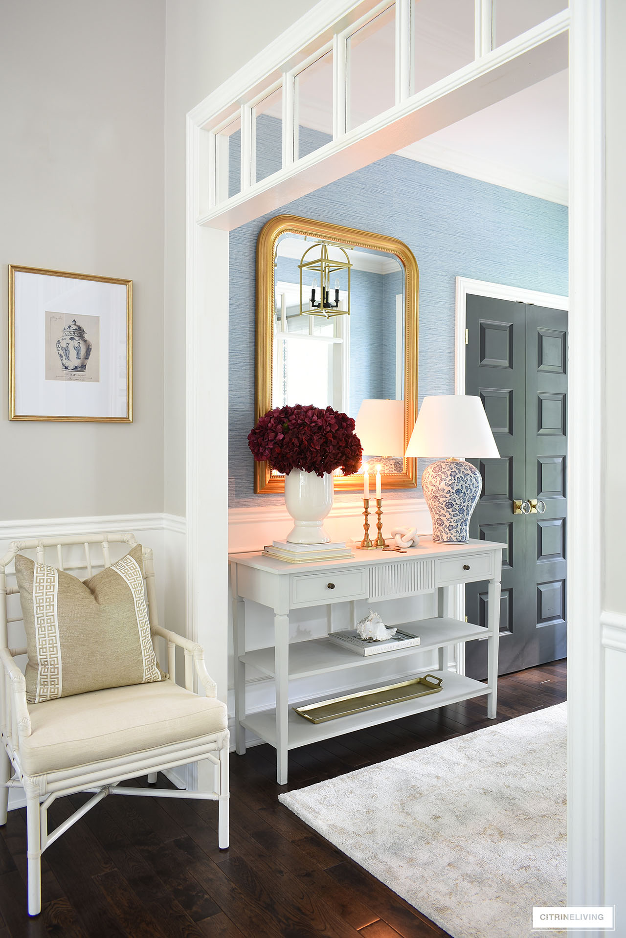 Entryway decorated for fall with burgundy hydrangeas gold accents and blue and white lamp 