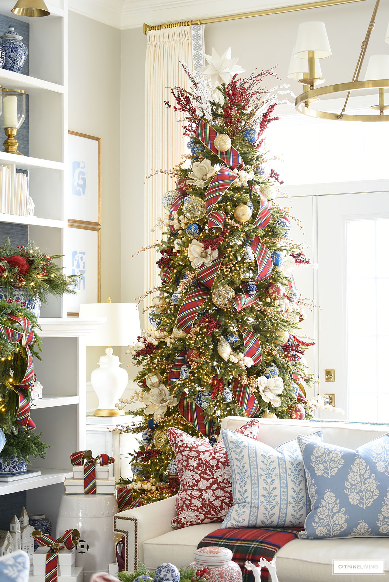 Christmas tree with plaid ribbon, throw pillows on white sofa.