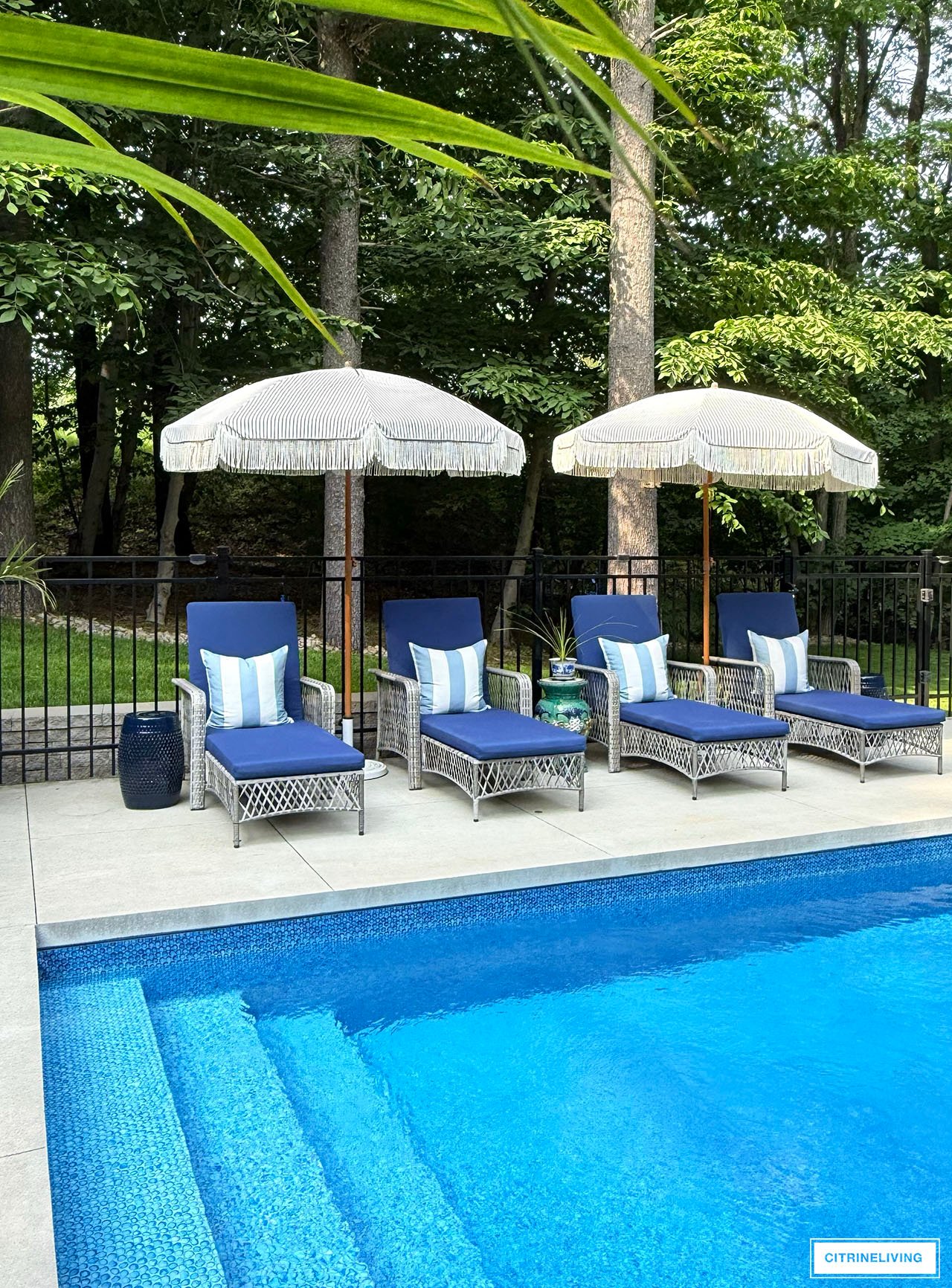 Pool loungers with navy cushions and striped throw pillows, umbrellas with fringe.