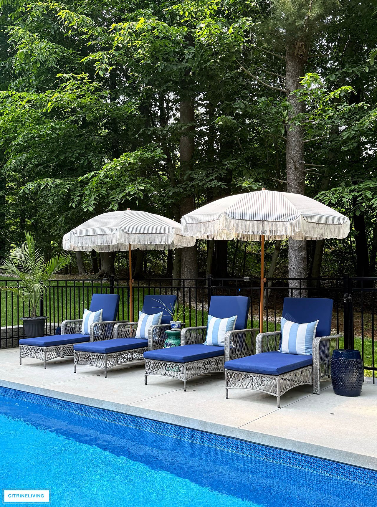 Pool loungers with navy cushions and striped throw pillows, umbrellas with fringe.